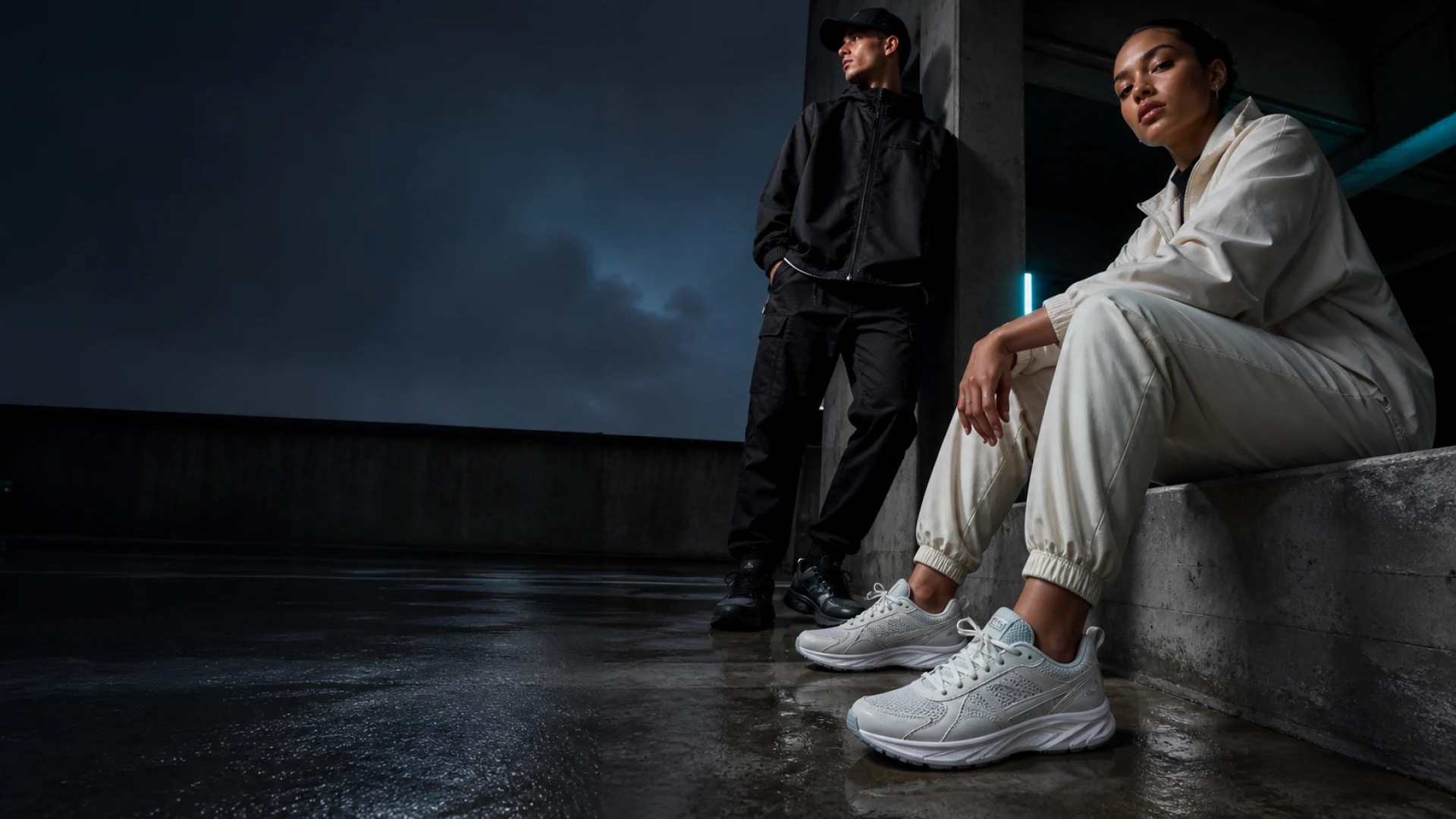 Two adults wearing modern streetwear and unbranded technical trainers in a dark urban setting